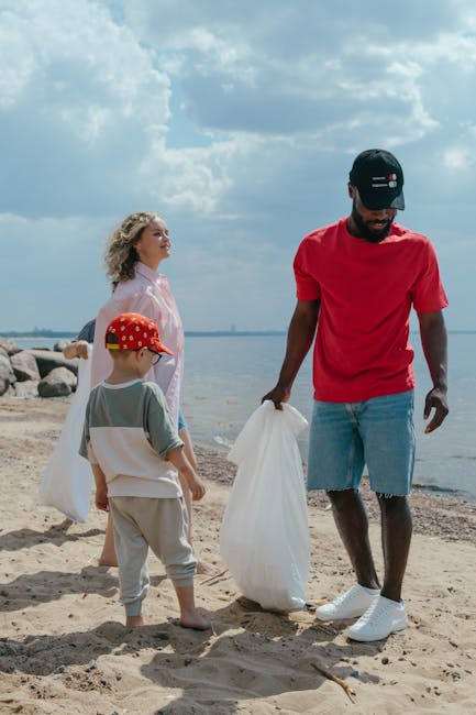 A person stands on a rocky shoreline near the water, wearing black shorts, a light blue shirt, and white sneakers with green accents. They are holding a grabber tool in one hand and a plastic bag in t